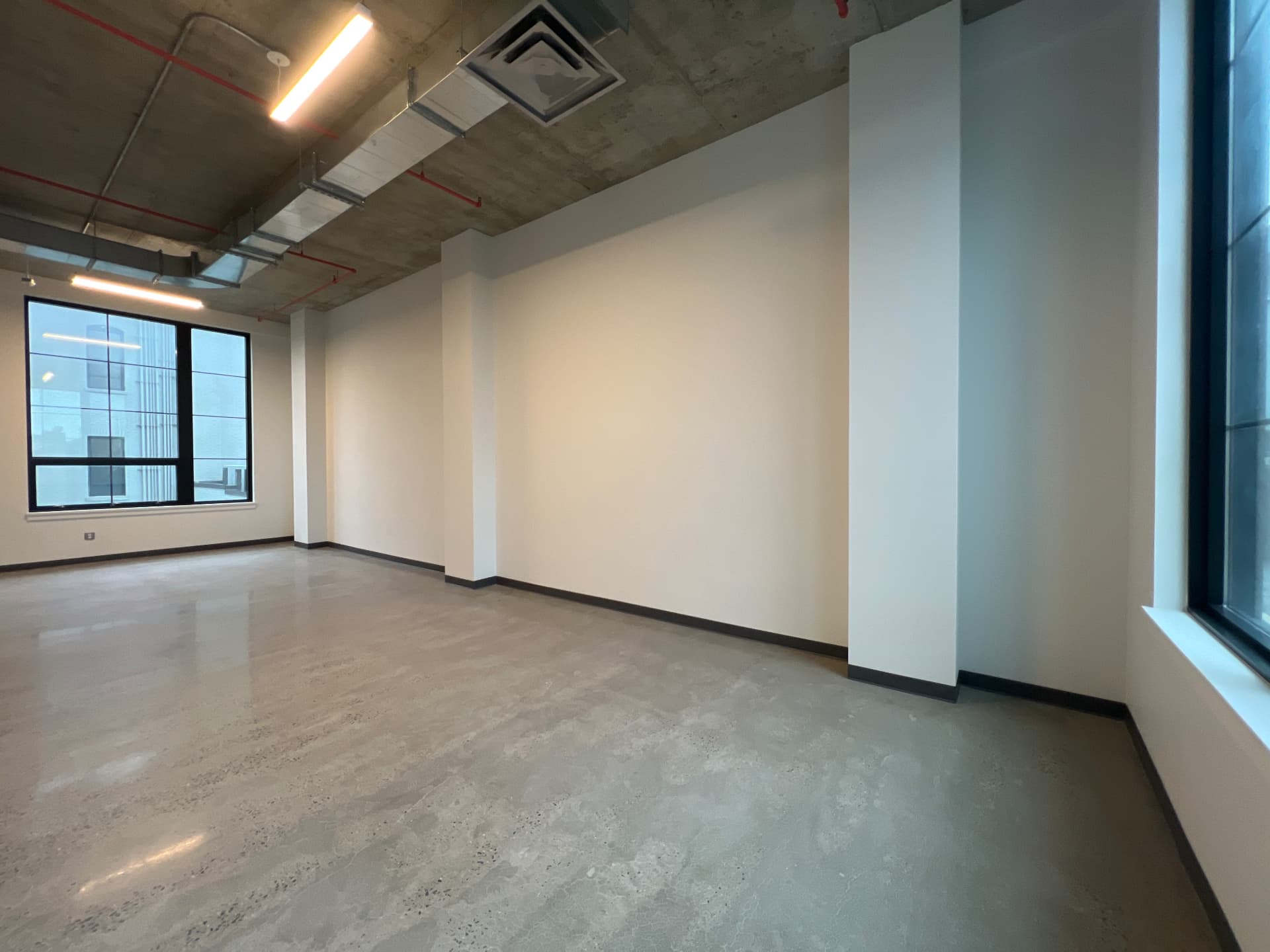 Corner of a divided suite with concrete floor, white walls and a black steel-framed window