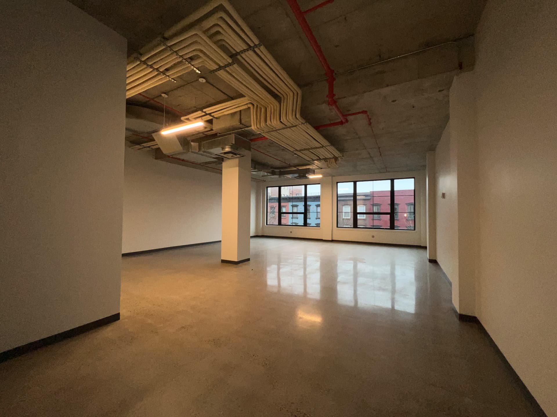 Open loft floor with white columns, exposed ceiling piping and windows facing brick townhouses