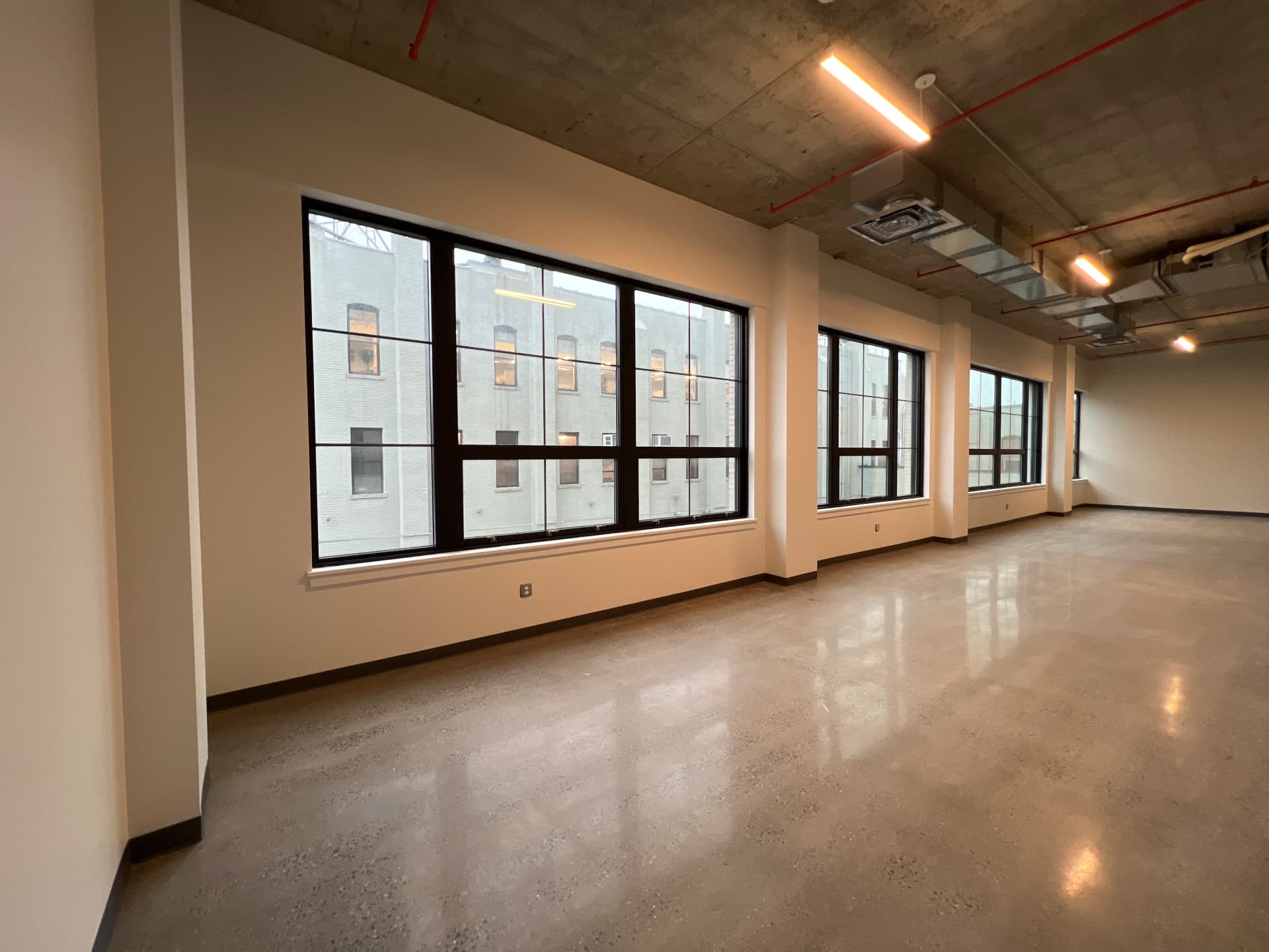 Window wall of a full-floor loft with exposed concrete ceiling and pendant lighting
